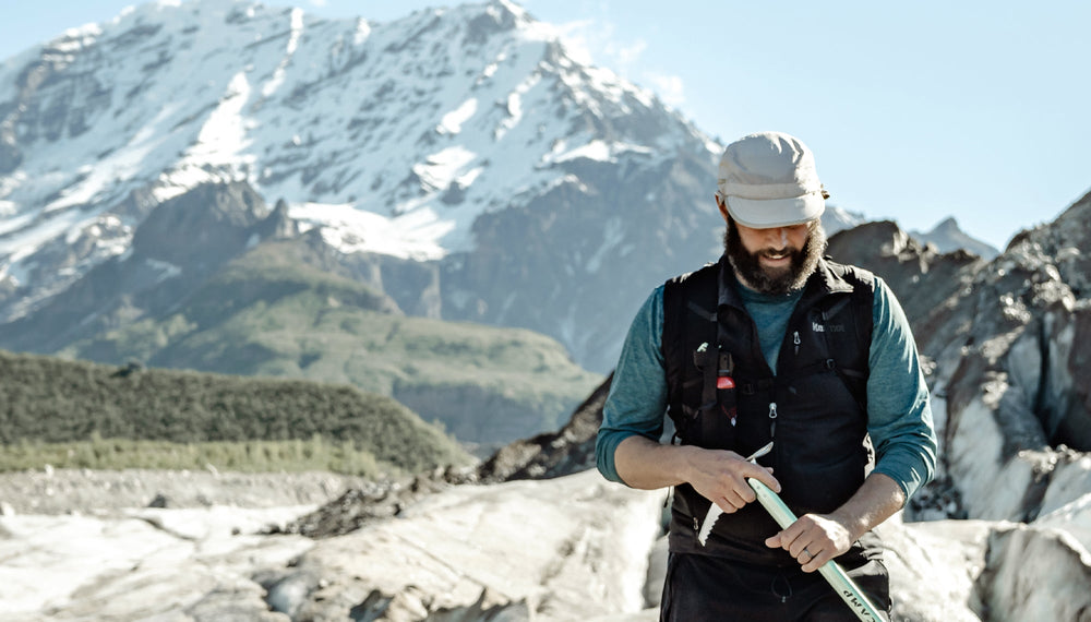 Man hiking in front of snowy mountain range, holding ice axe