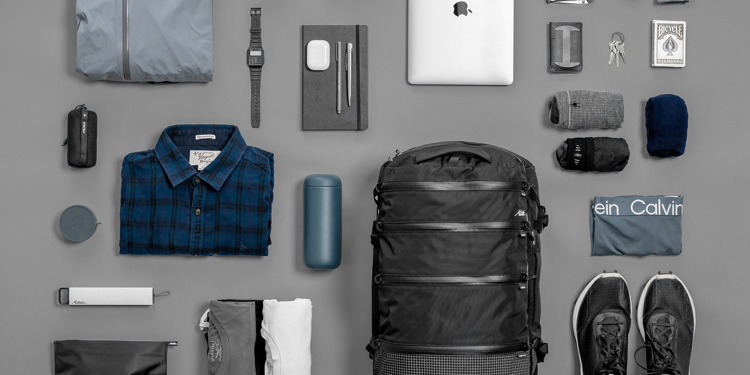 SEG28 laid flat on gray background with contents like clothing, laptop, sunglasses, snacks, and toiletries