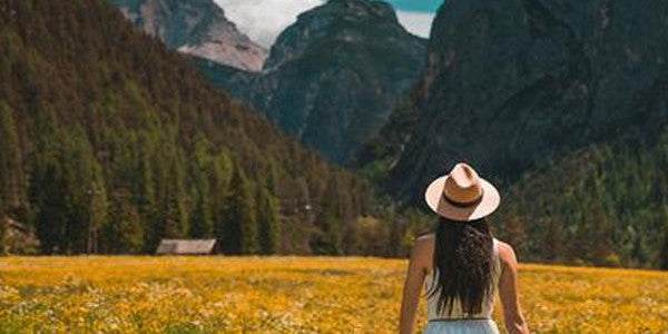 Woman in hat, standing in golden field with mountains in the background