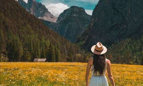 Woman in hat, standing in golden field with mountains in the background