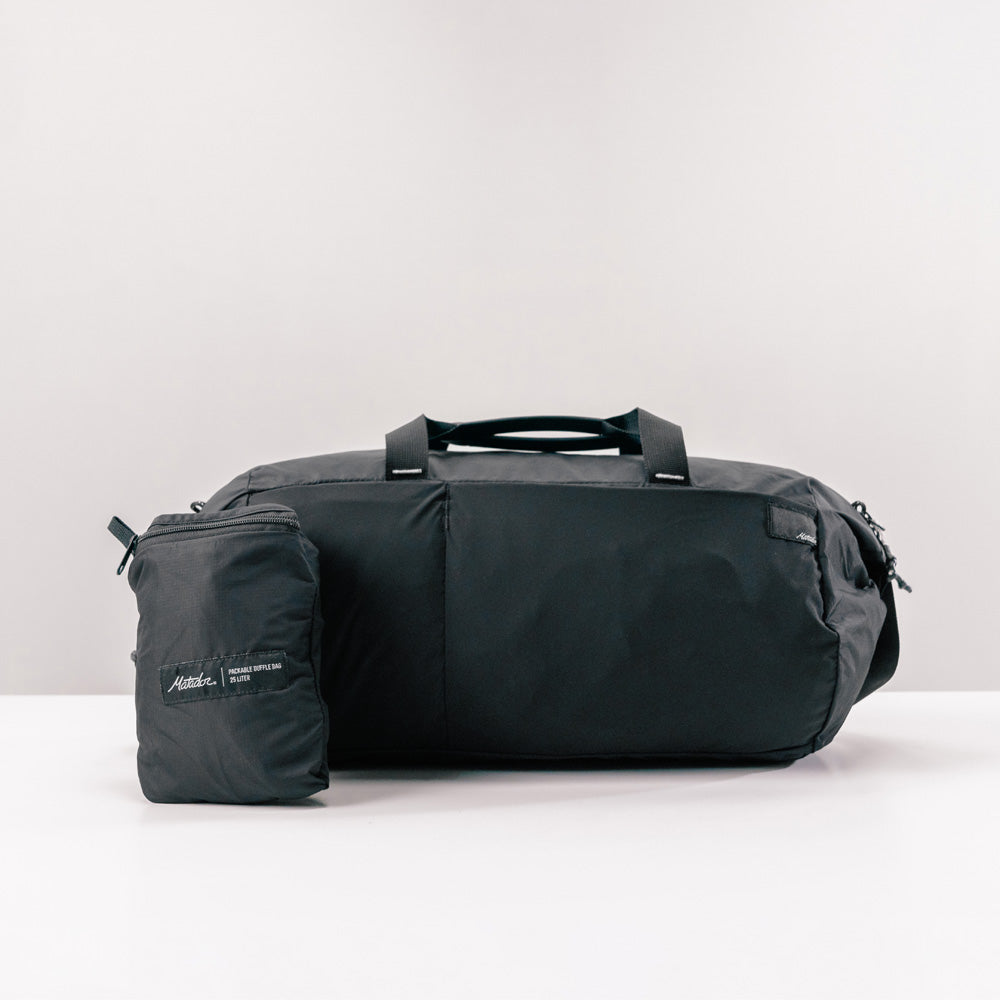 black duffle and packed up duffle on light gray background