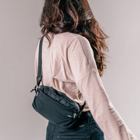 woman on light gray background wearing black sling bag across the back of her body