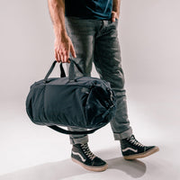 man holding black duffle by the straps at his side