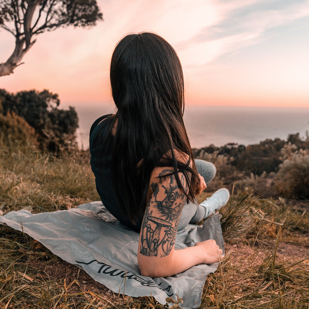 Woman laying on Pocket Blanket Mini overlooking an ocean sunset