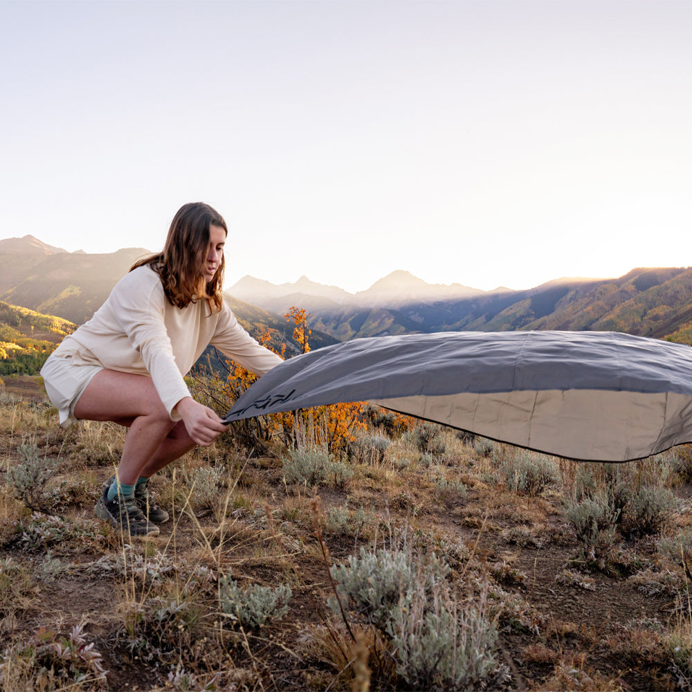 Woman in mountain sunset scene, laying down pocket blanket on dry brush