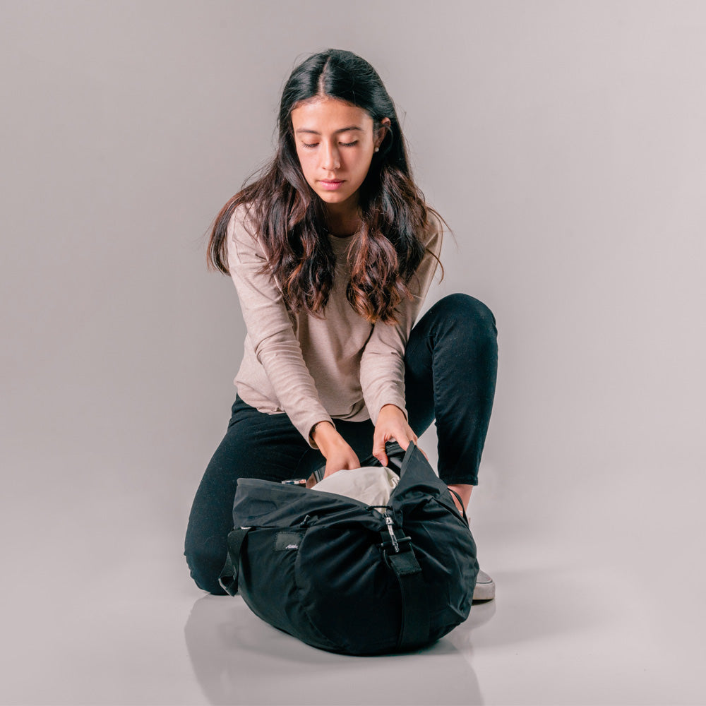 woman placing clothing in open black duffle sitting on the ground