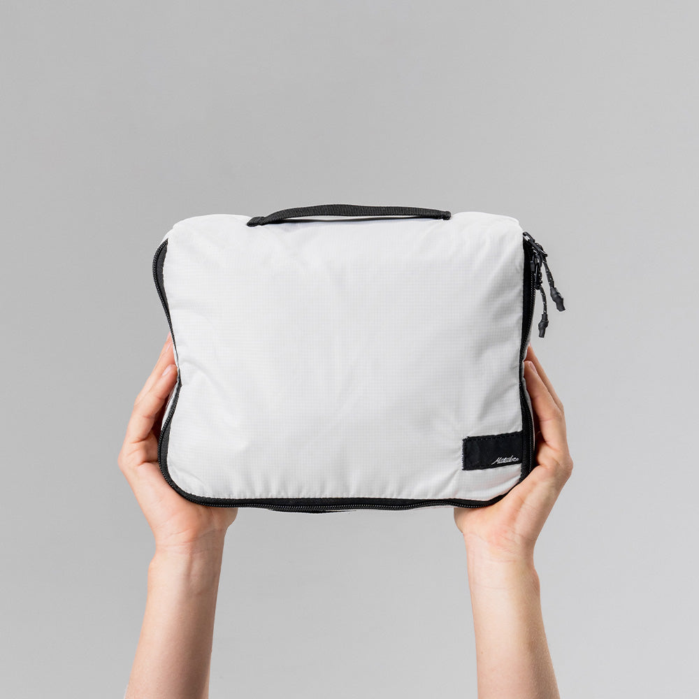 Hands holding white packing cube in front of light gray background