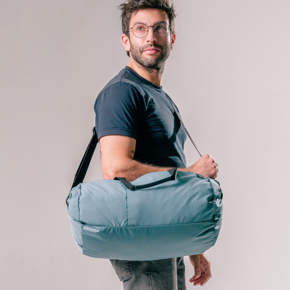 man wearing slate blue duffle over his shoulder and across his body