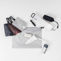 Flat lay of travel toiletries including FlatPak toiletry bottle, pill container, toothbrush with cap and other toiletry items.