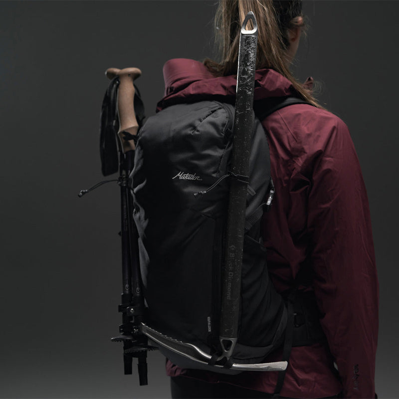 3/4 view of Woman wearing Beast18 with hiking poles and ice axe on gray background