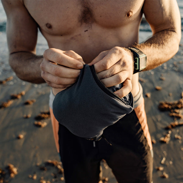 Man standing on beach, unzipping packed up charcoal poncho