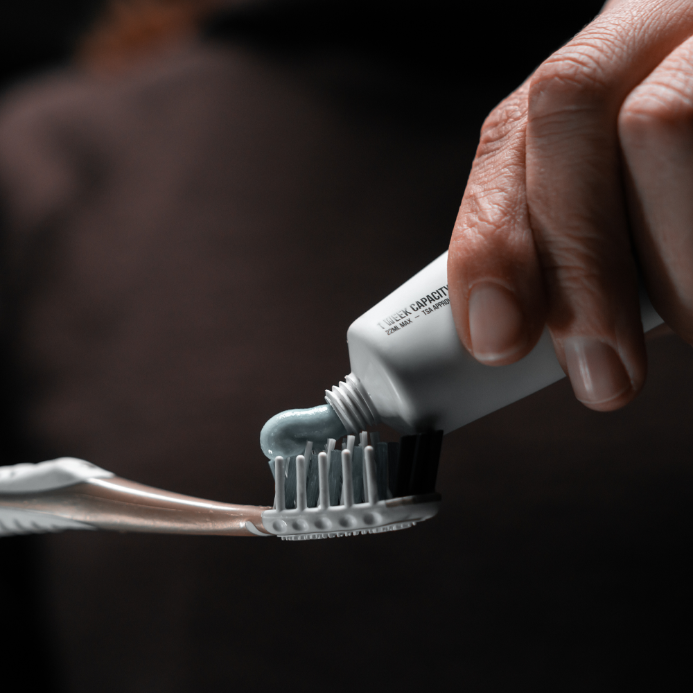 hands on black background squeezing toothpaste from white toothpaste tube onto gold toothbrush