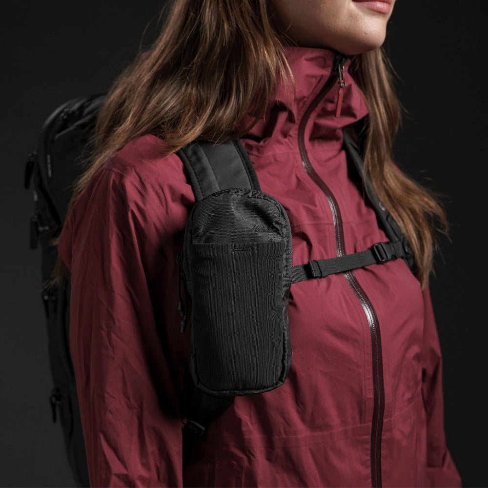 Side view of woman in burgundy jacket, wearing speed stash on her backpack strap