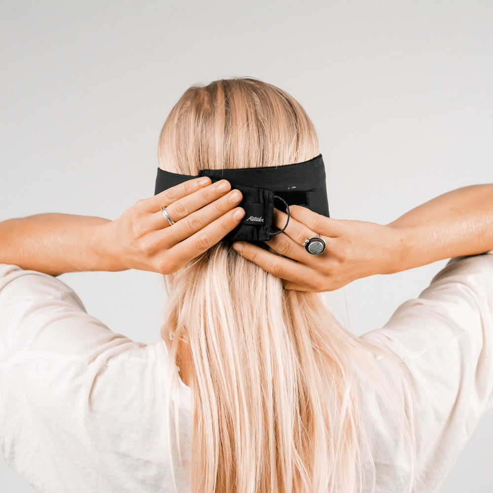 Back view of woman on light gray background, securing eye mask behind her head