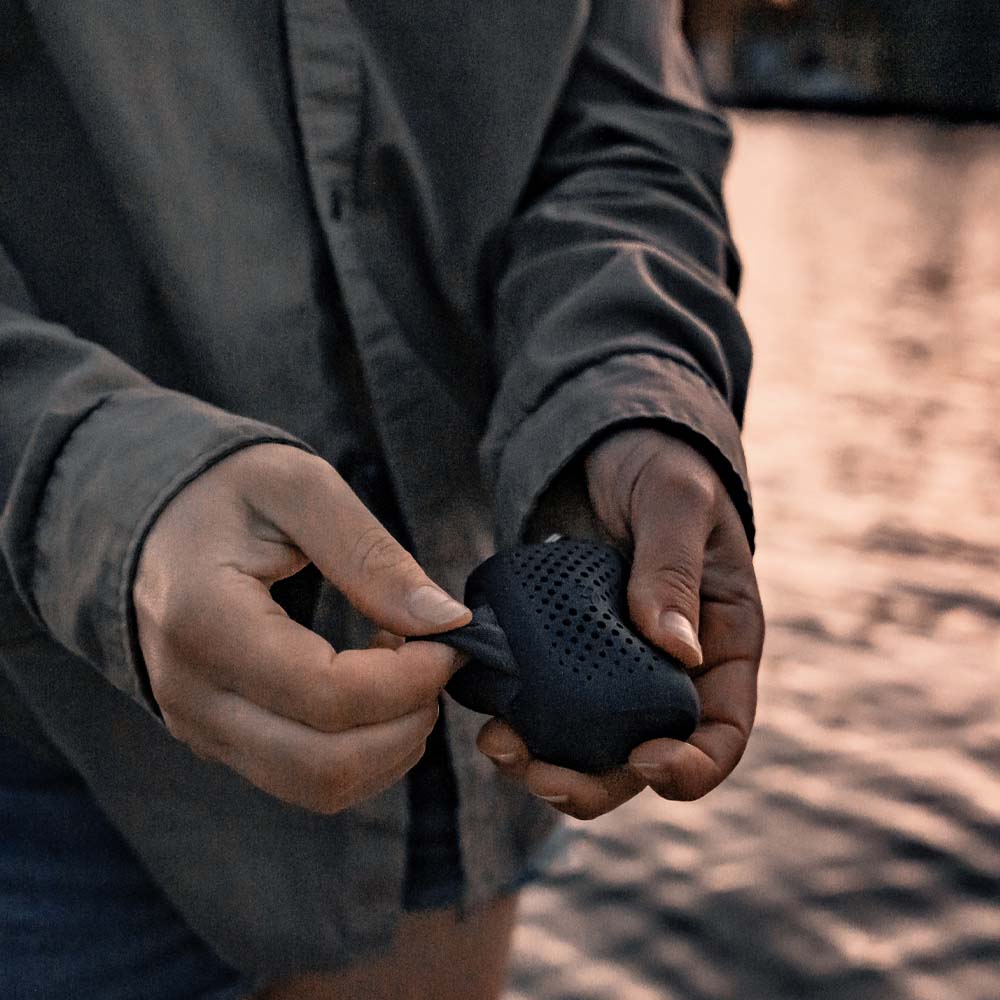 Woman at sunset lake, pulling NanoDry Trek Towel out of its silicone case