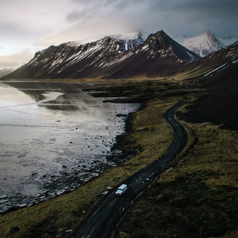 White landrover driving down winding lakeshore road, with snowy mountain top backdrop