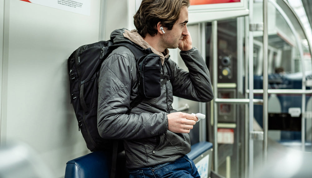 man in train, wearing speed stash on his backpack strap