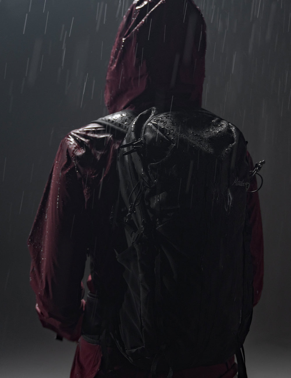 person in dark, rainy setting, wearing black backpack