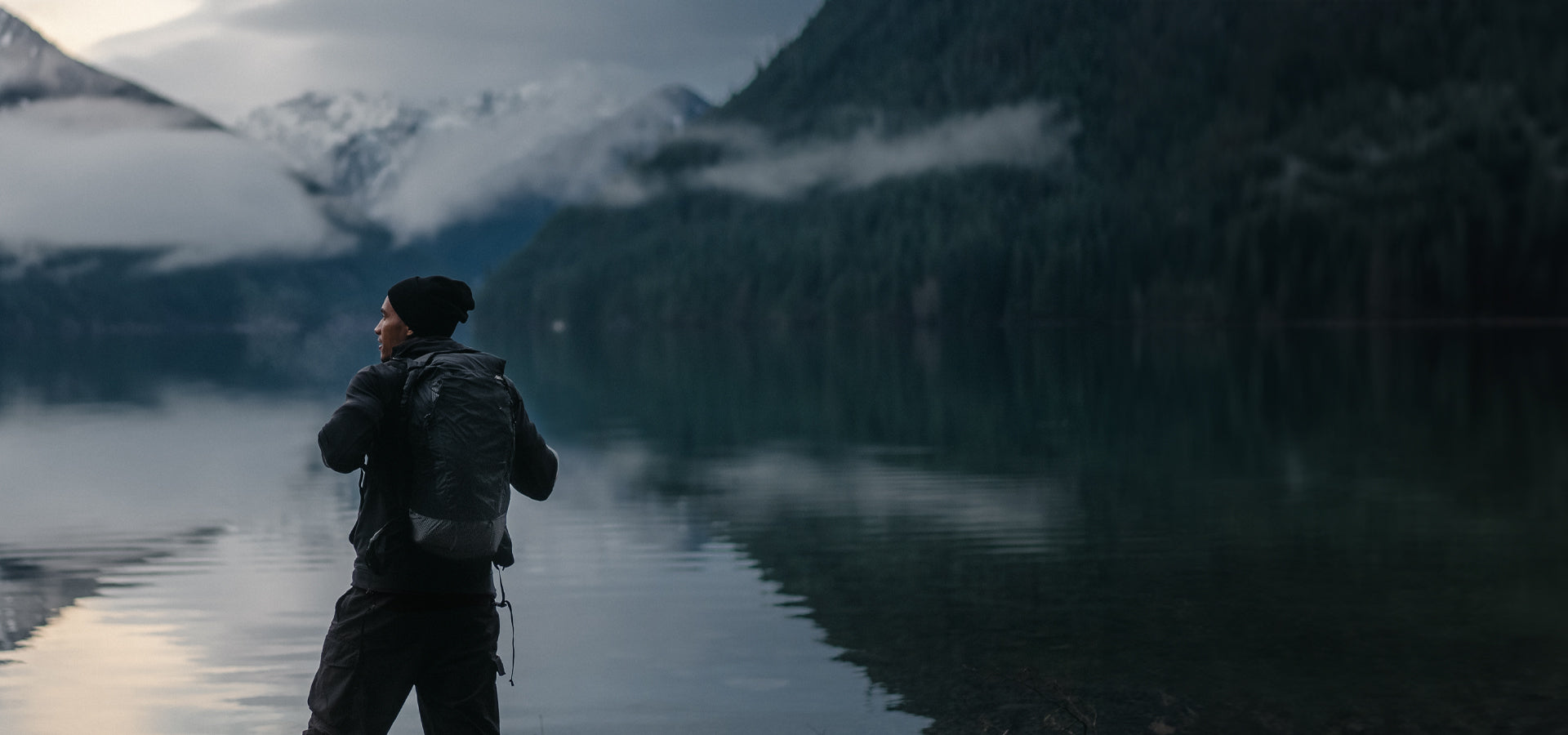 Man standing in front of moody alpine lake