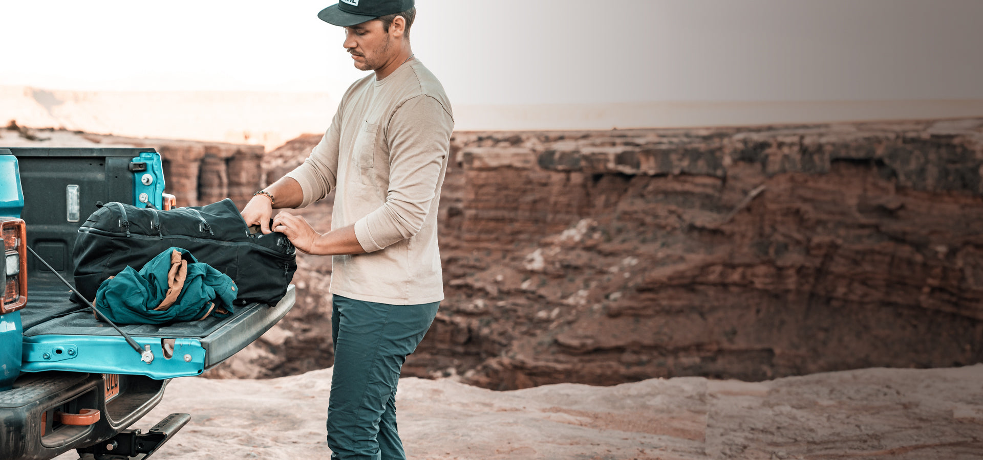 man at canyon rim digging through his black SEG45 pack in the bed of a truck