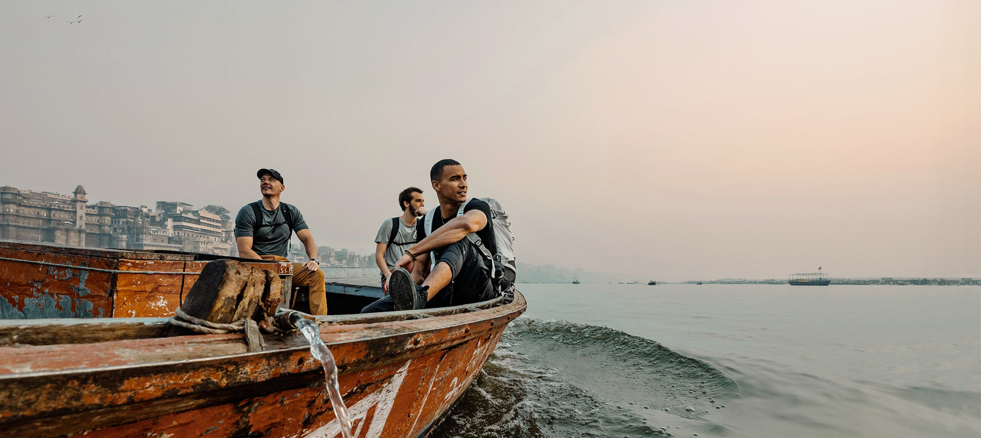 Three men in a weathered rowboat, looking out at Indian sunset 