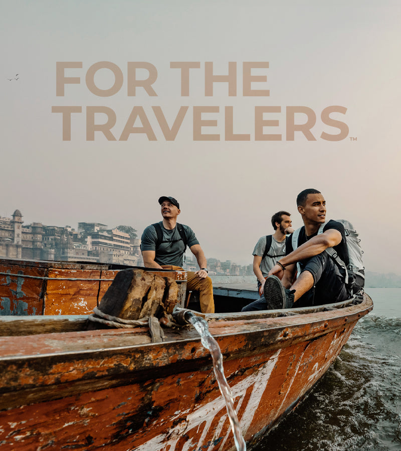 Two men in a weathered rowboat, looking out at Indian sunset with text that reads "For the Travelers"