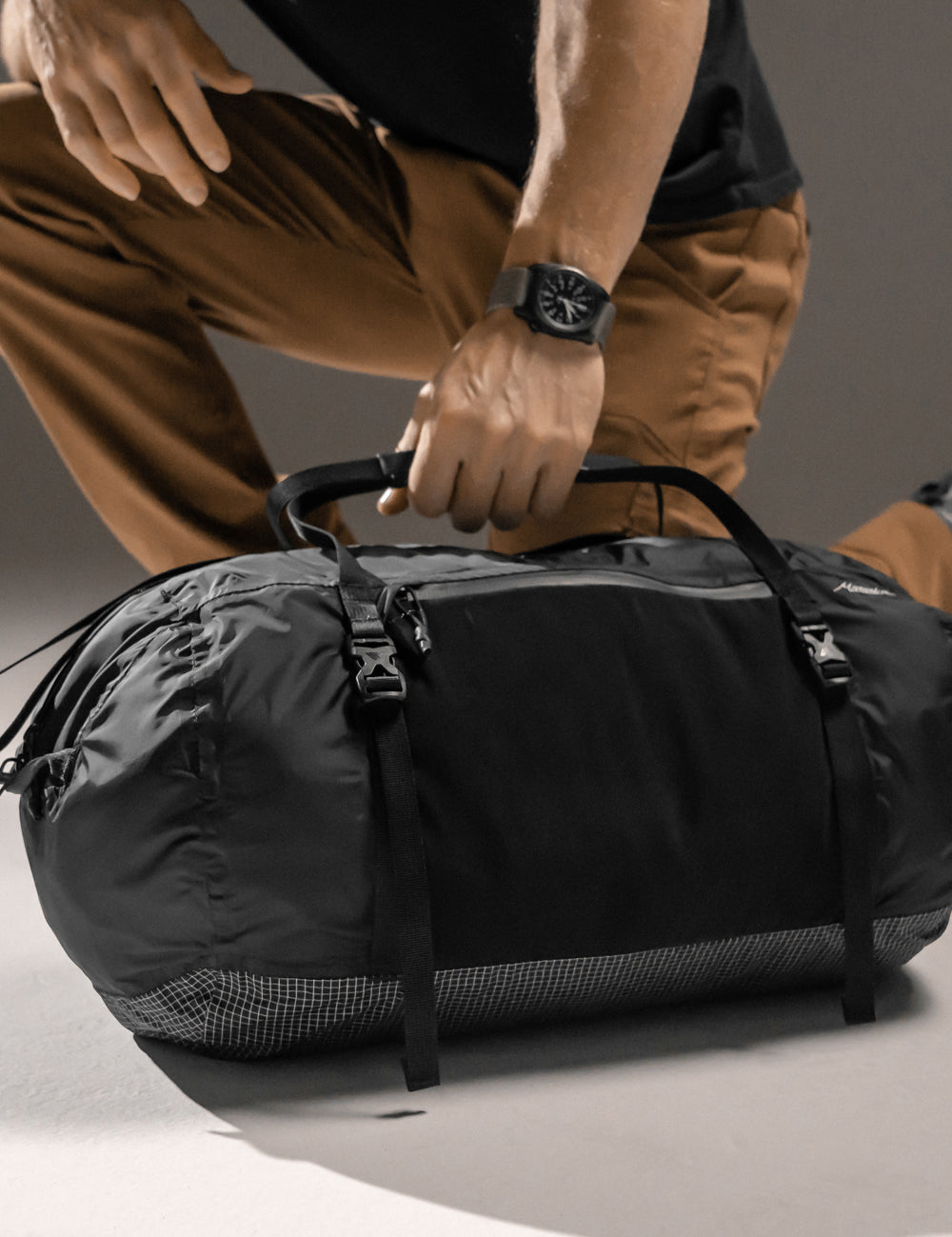 man kneeling next to black duffle