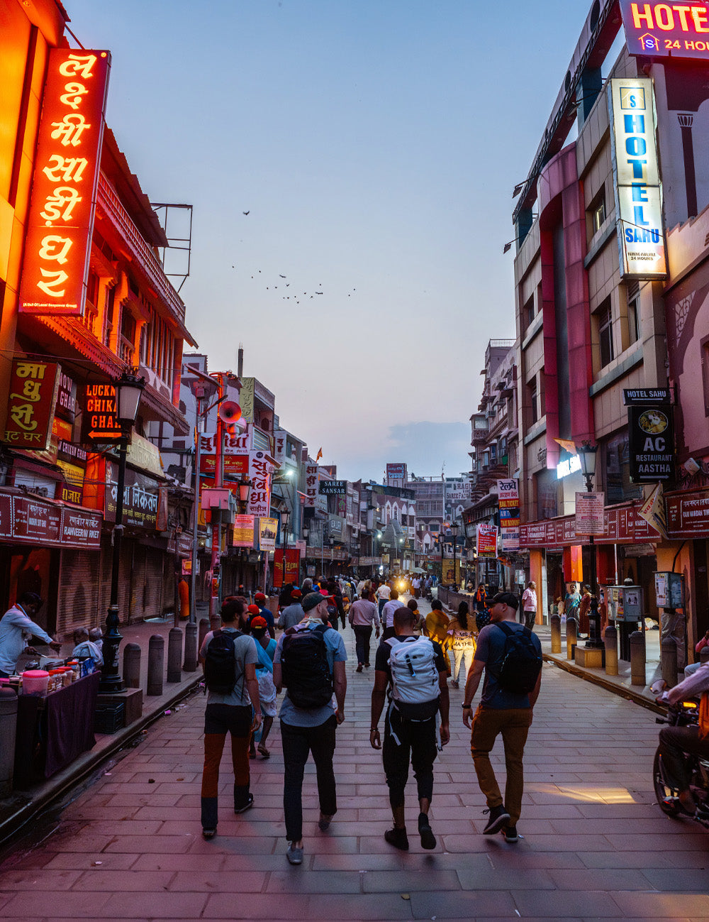 4 men walking down Indian street lit up by neon lights