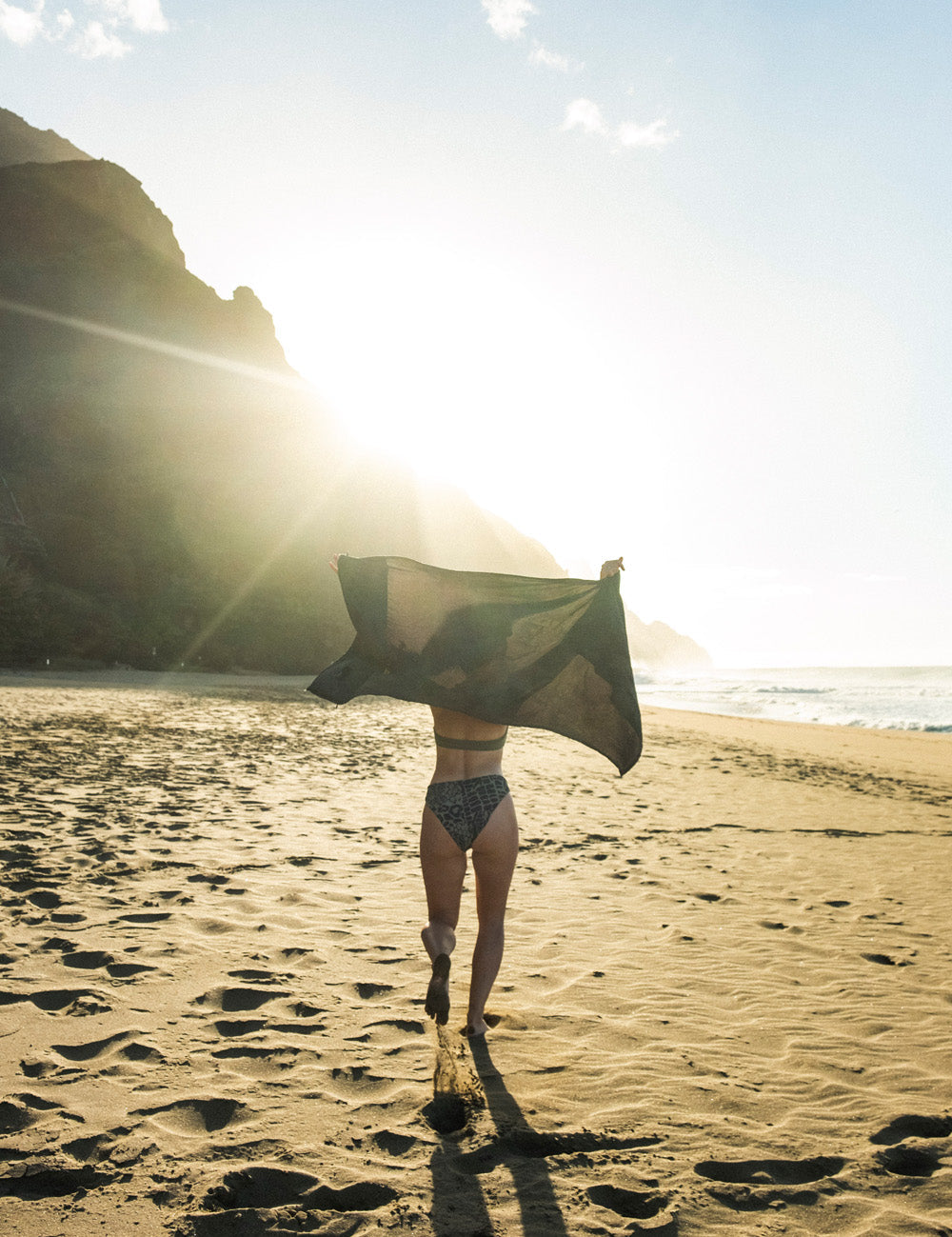woman running along sunset beach holding towel in the wind