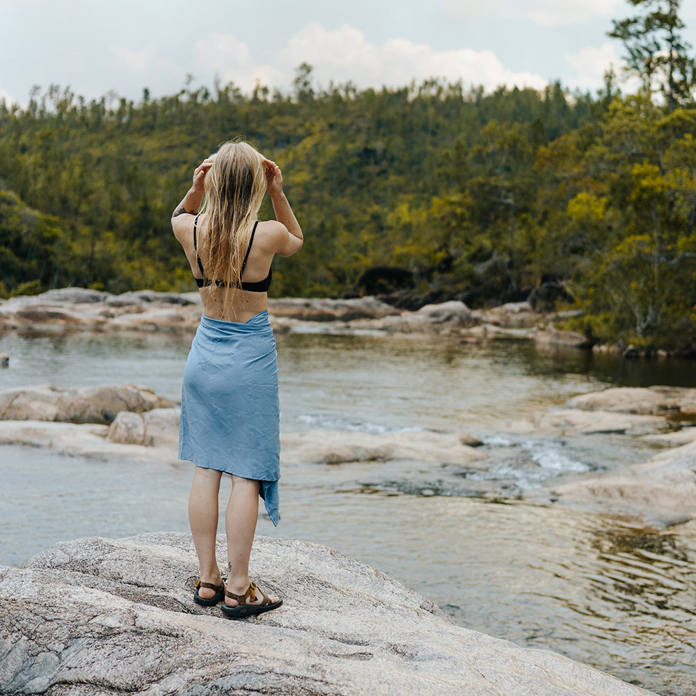 woman on rocky shore wearing blue towel around her waist