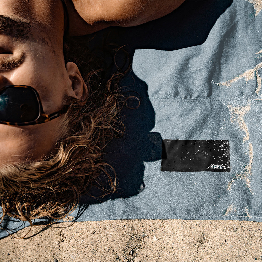 top down view of man laying on matador beach towel in sand