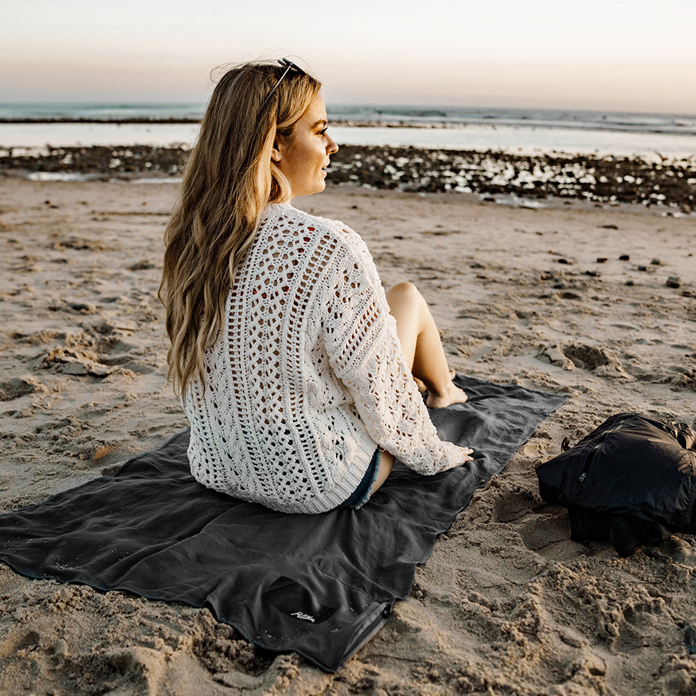 woman on sandy beach, sitting on towel