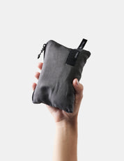 Hand holding a gray fabric pouch with a black zipper on a white background