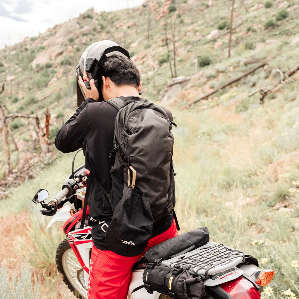 man in deserty landscape, sitting on motorcycle wearing black backpack