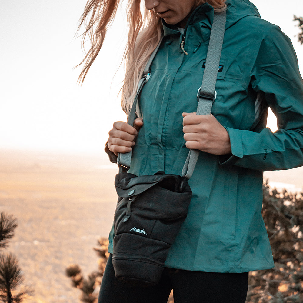 Woman on mountainside with camera base layer hanging from her camera strap