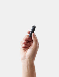 Hand holding a small black earplug case against a light background