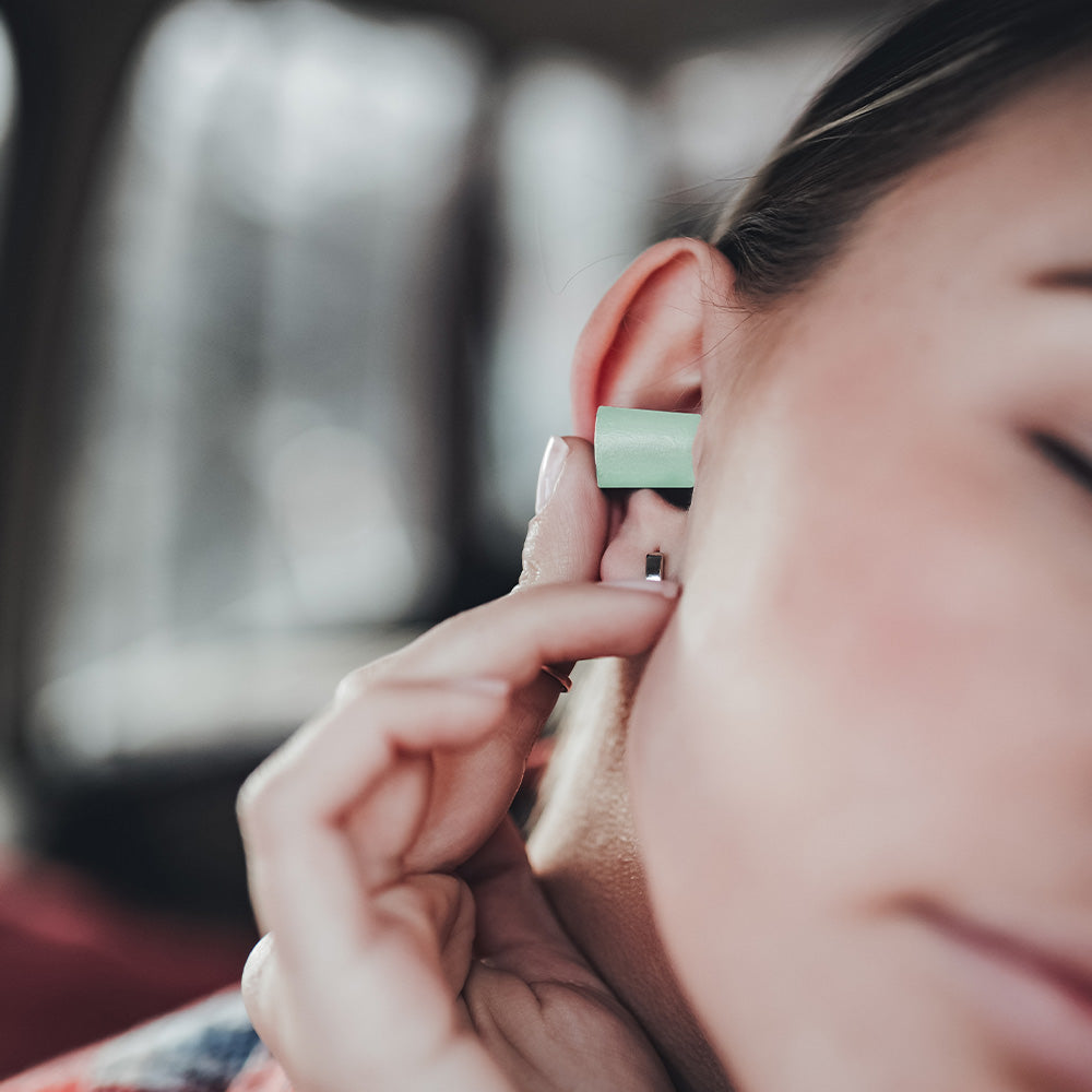 close up view of mint colored earplug being place in womans ear