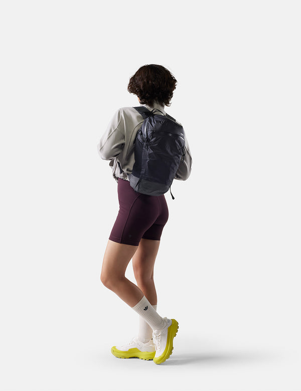 Person wearing a gray jacket, purple shorts, white socks, and yellow shoes with a black backpack on a white background