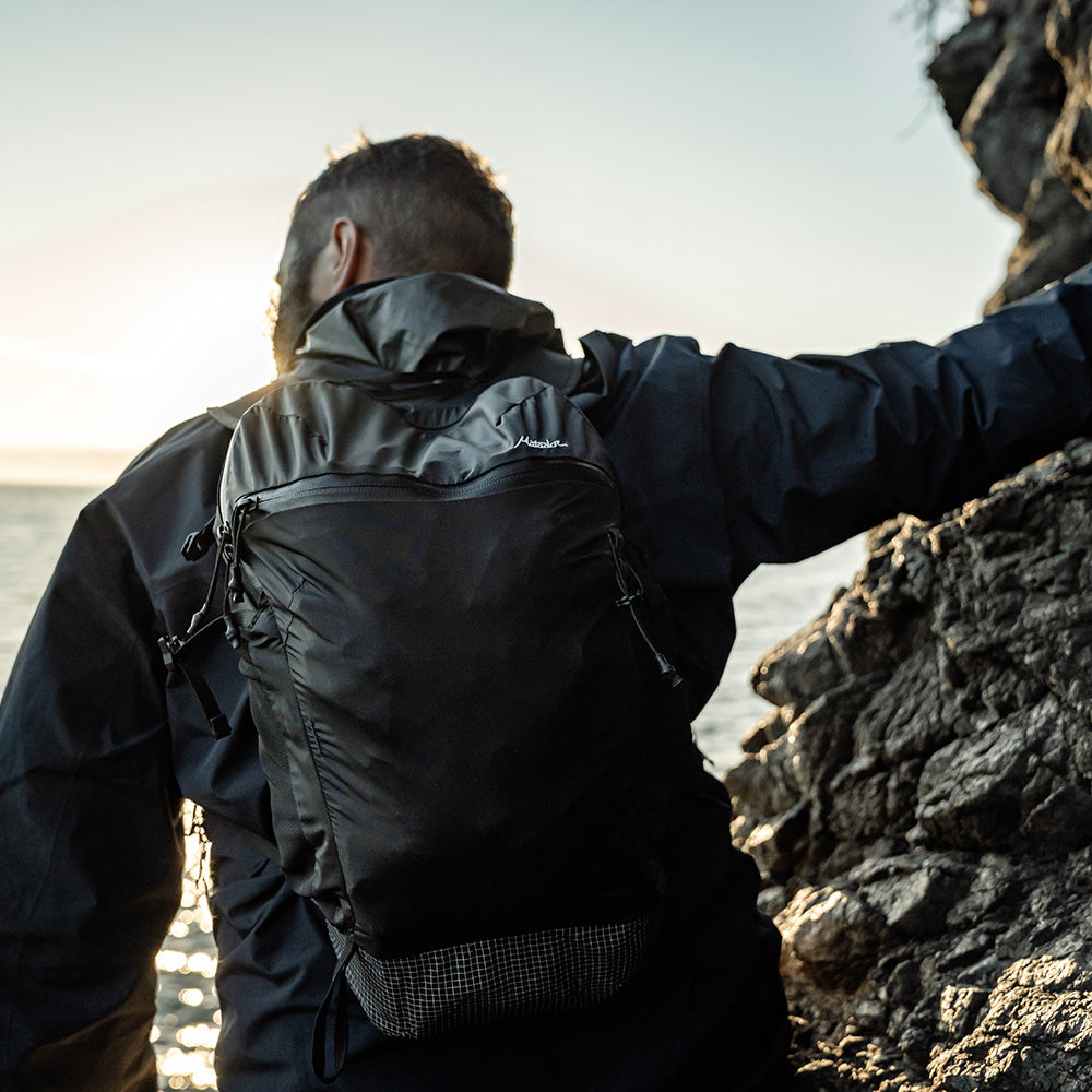 man looking out at rocky sea wearing black backpack