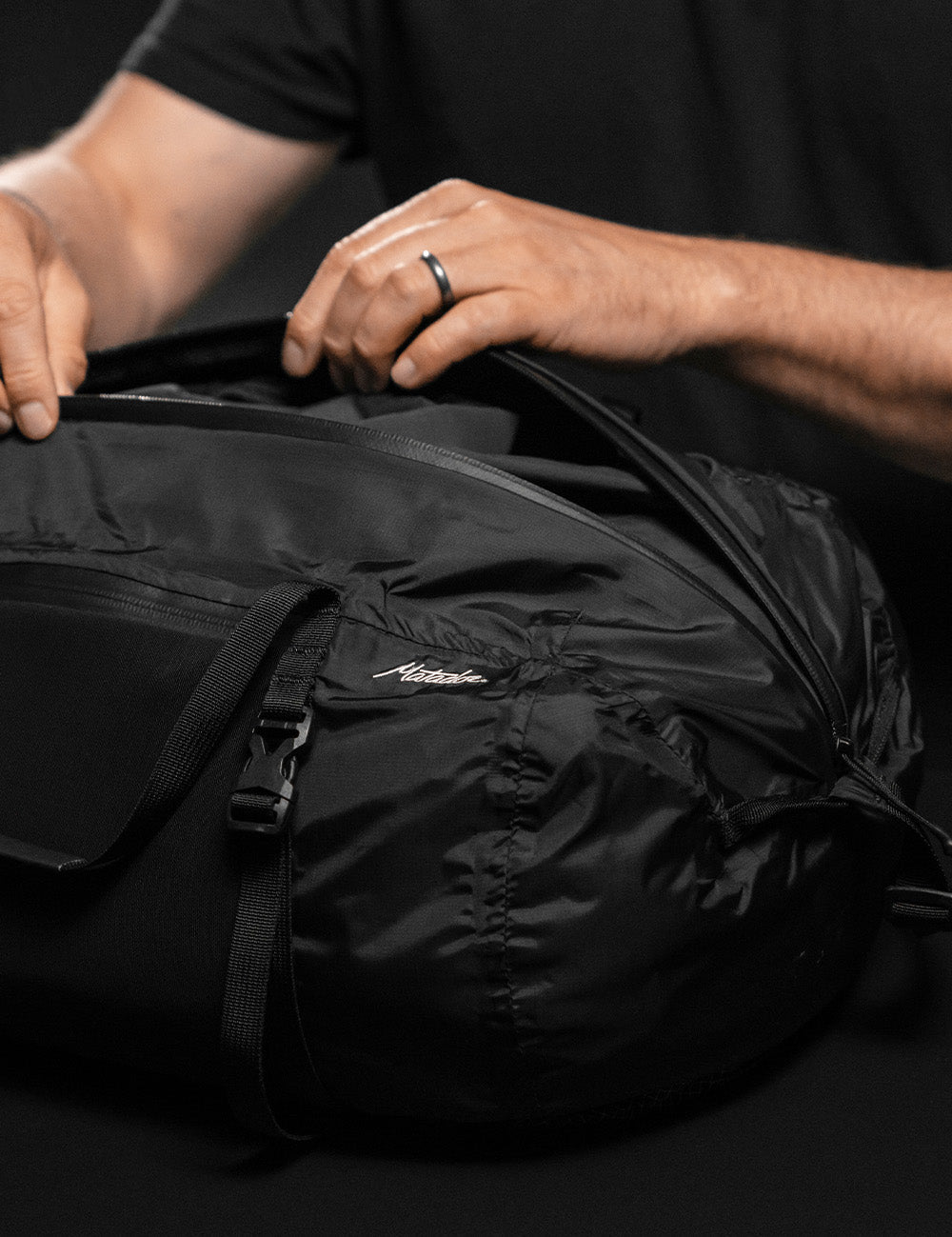 hands opening black duffle with extra long zipper
