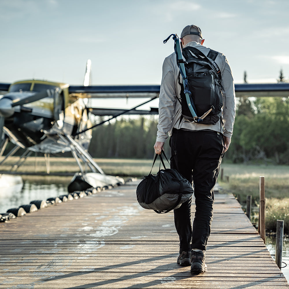 man carrying duffle while walking on dock to sea plane