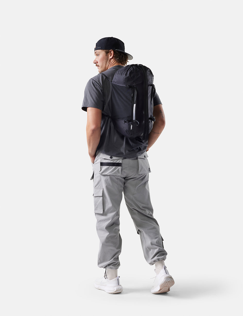 Person wearing a black backpack and gray pants on a white background