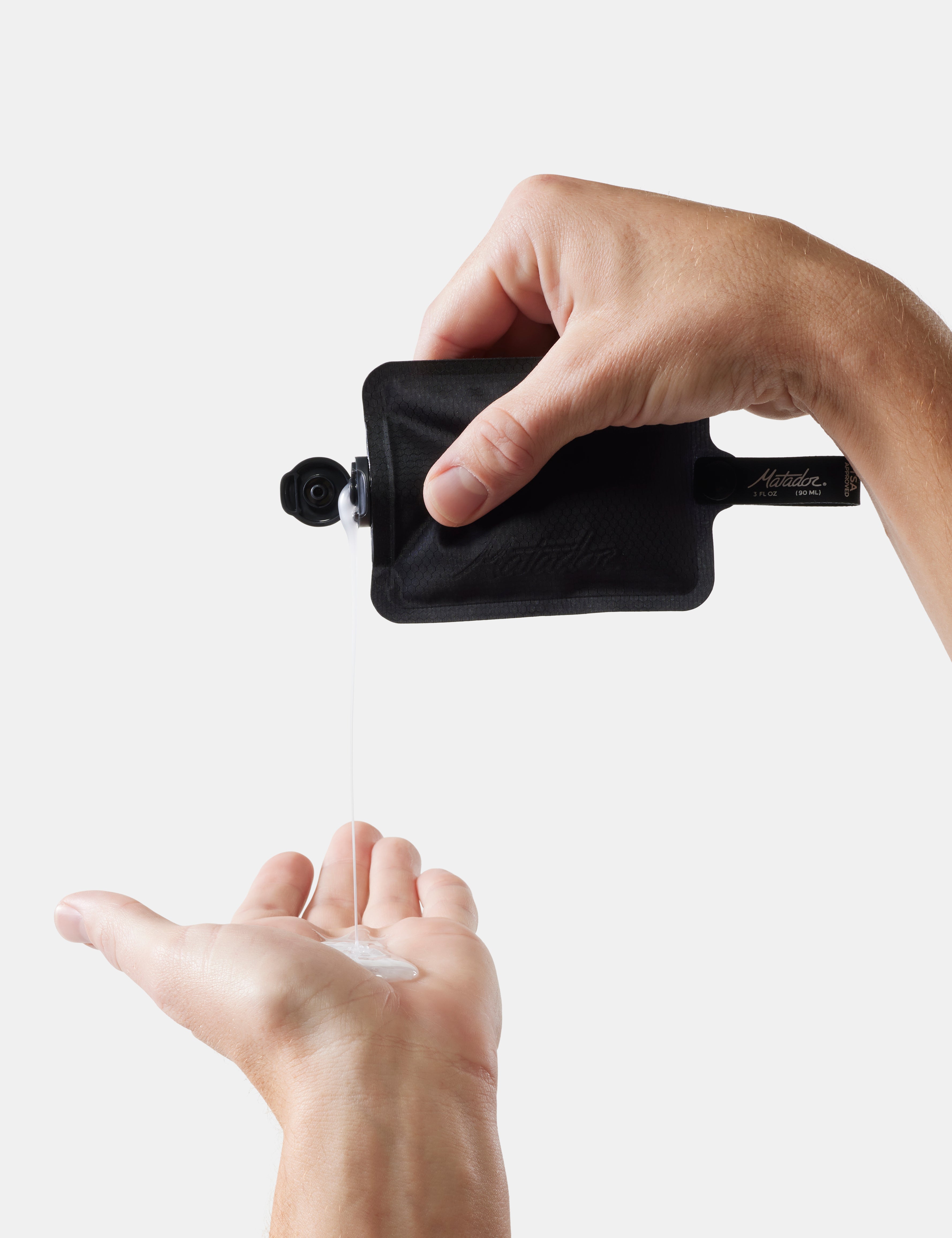 Hand using a black travel-sized bottle to dispense liquid soap into another hand on a white background