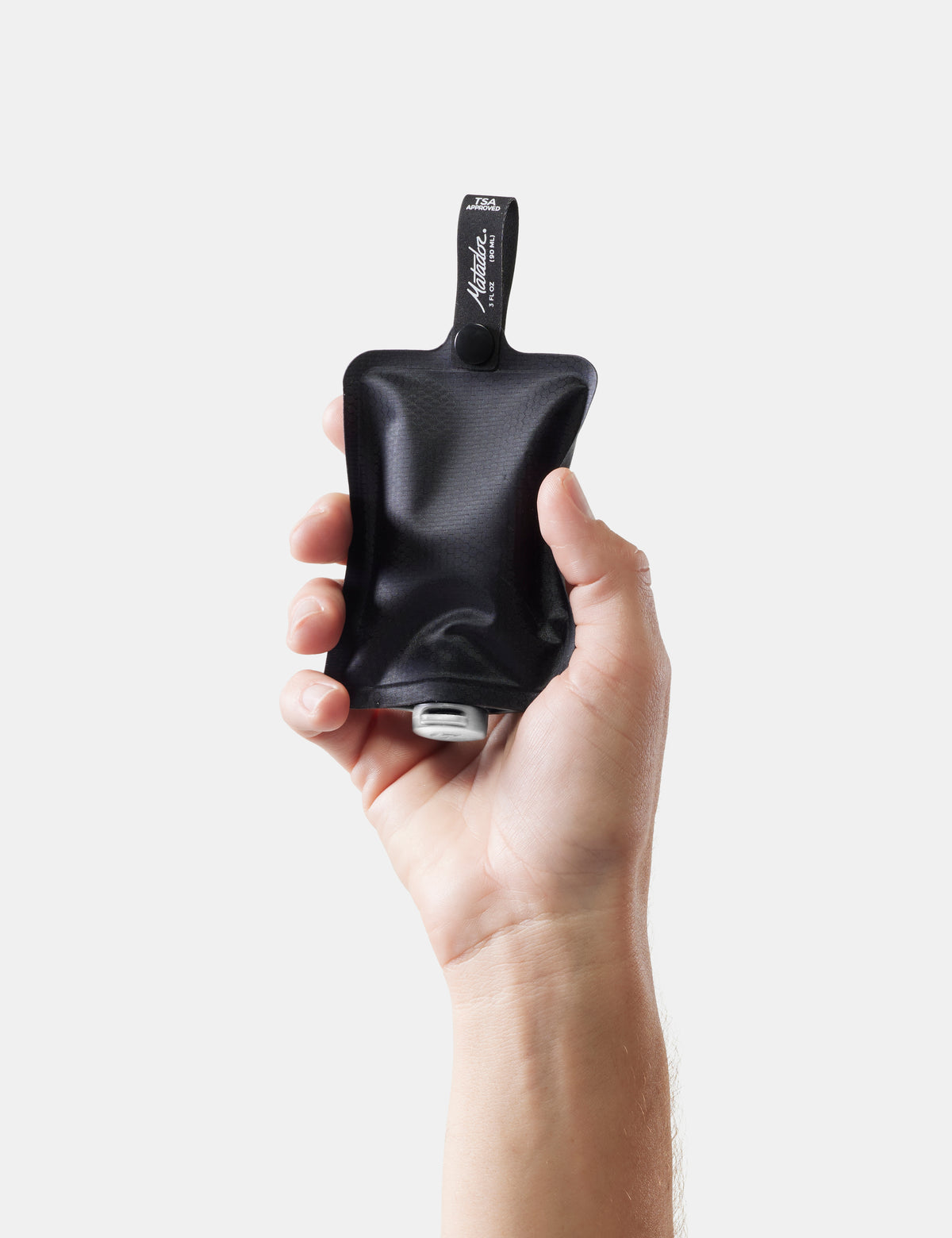 Hand holding a black toiletry bottle with a brand label on a white background