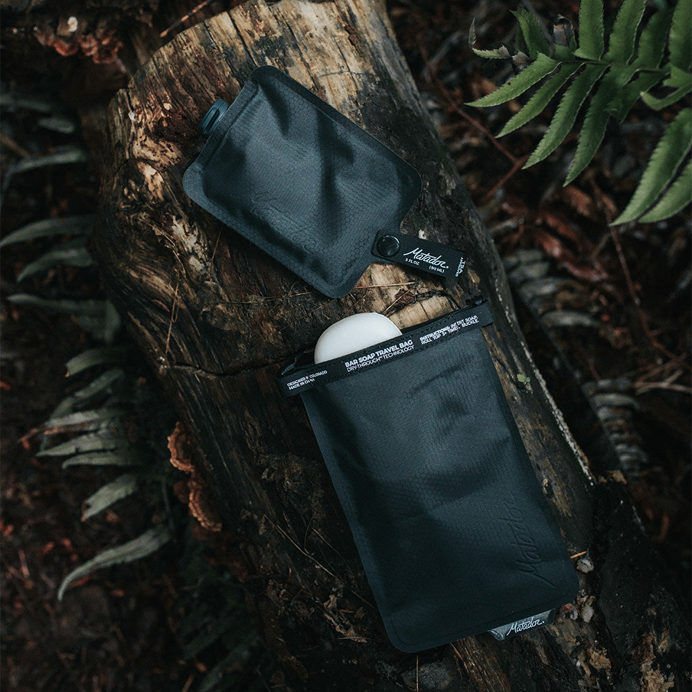 soap bar case and toiletry bottle sitting on log