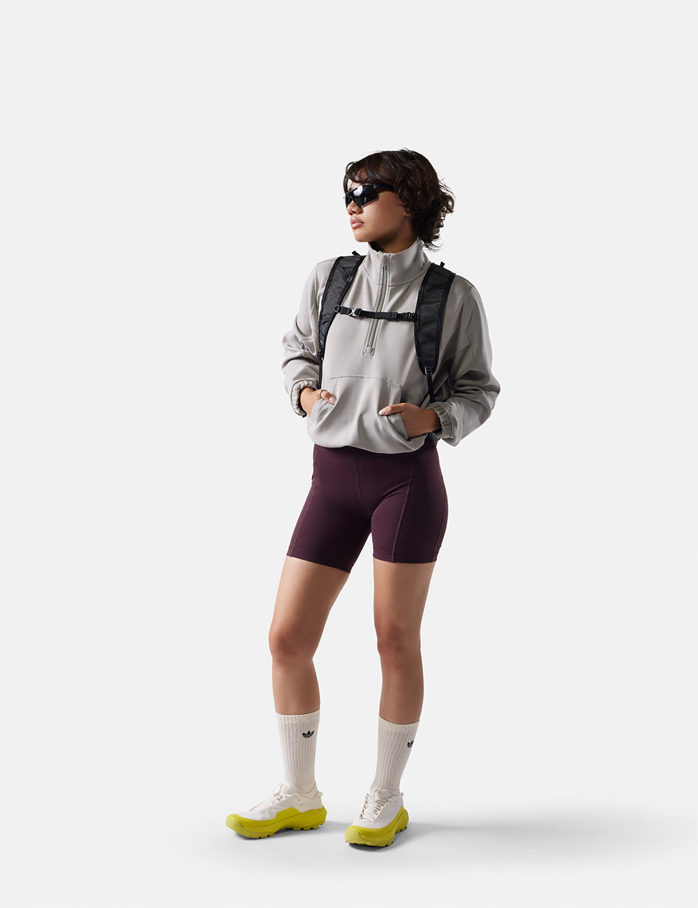 Person wearing a gray jacket, maroon shorts, and white socks with a backpack on a white background