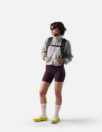 Person wearing a gray jacket, maroon shorts, and white socks with a backpack on a white background