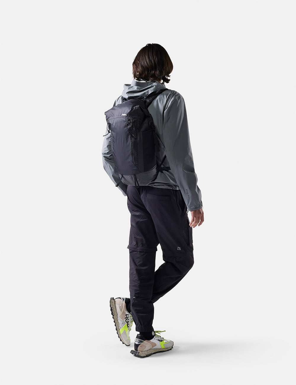 Person wearing a gray raincoat and black pants with a backpack on a white background