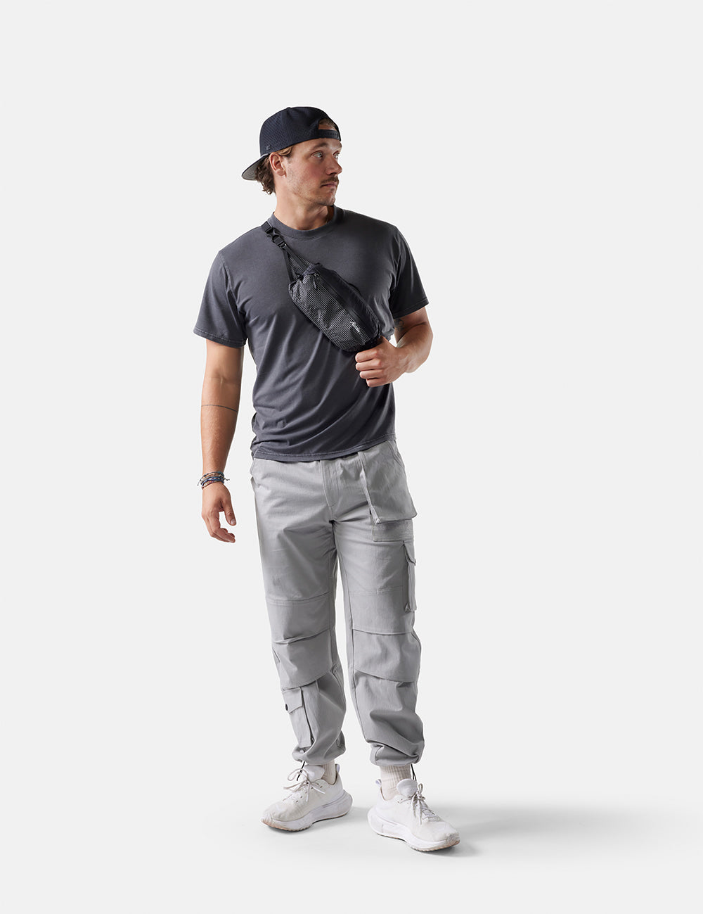 Man wearing a dark t-shirt, gray cargo pants, and a black cap on a white background