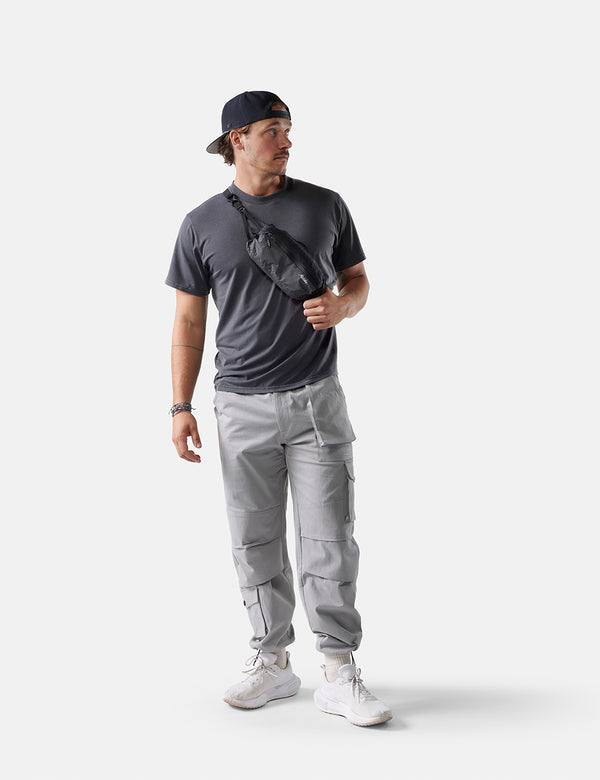 Man wearing a dark t-shirt, gray cargo pants, and a black cap on a white background